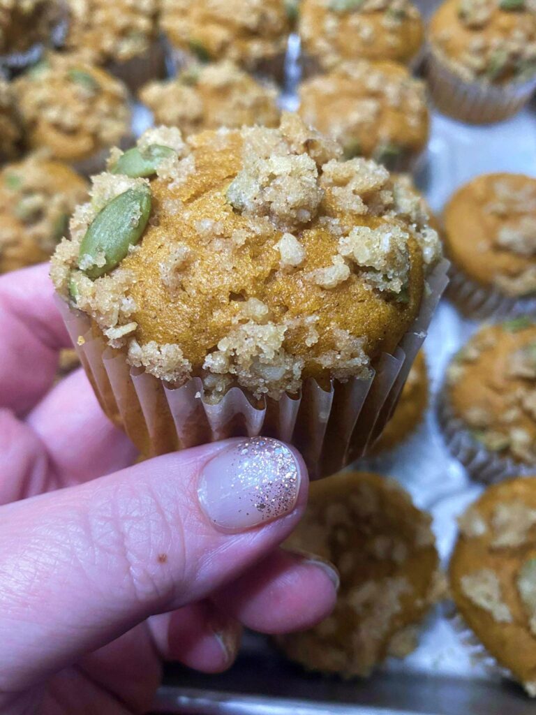 A hand holding a single pumpkin muffin.
